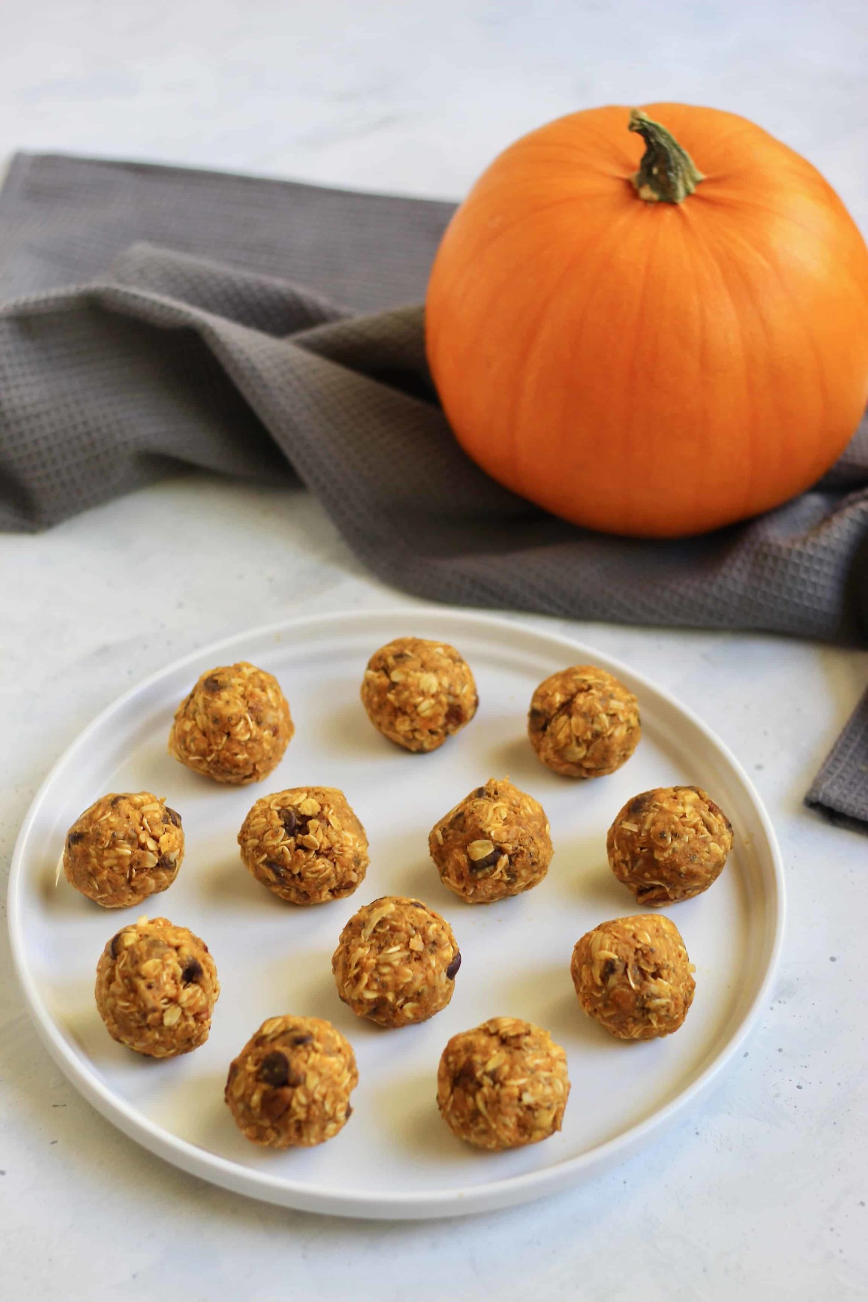 Pumpkin energy balls on a white plate with pumpkin in background