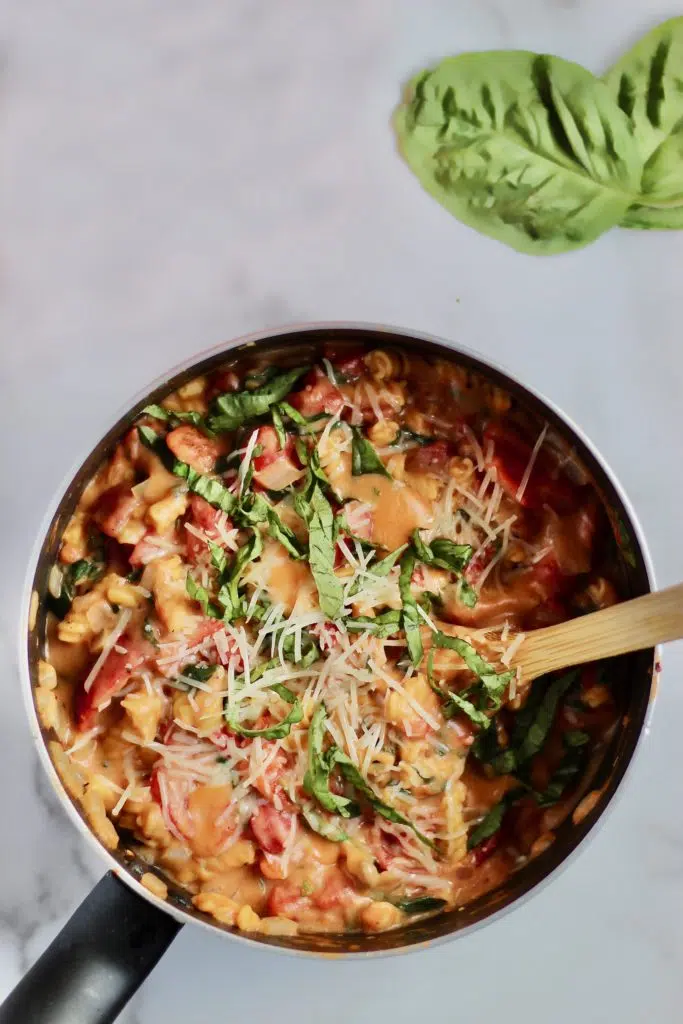 One Pot Tomato Basil Chickpea Pasta: A bowl of vibrant pasta with chickpea noodles, topped with fresh basil and grated parmesan cheese.