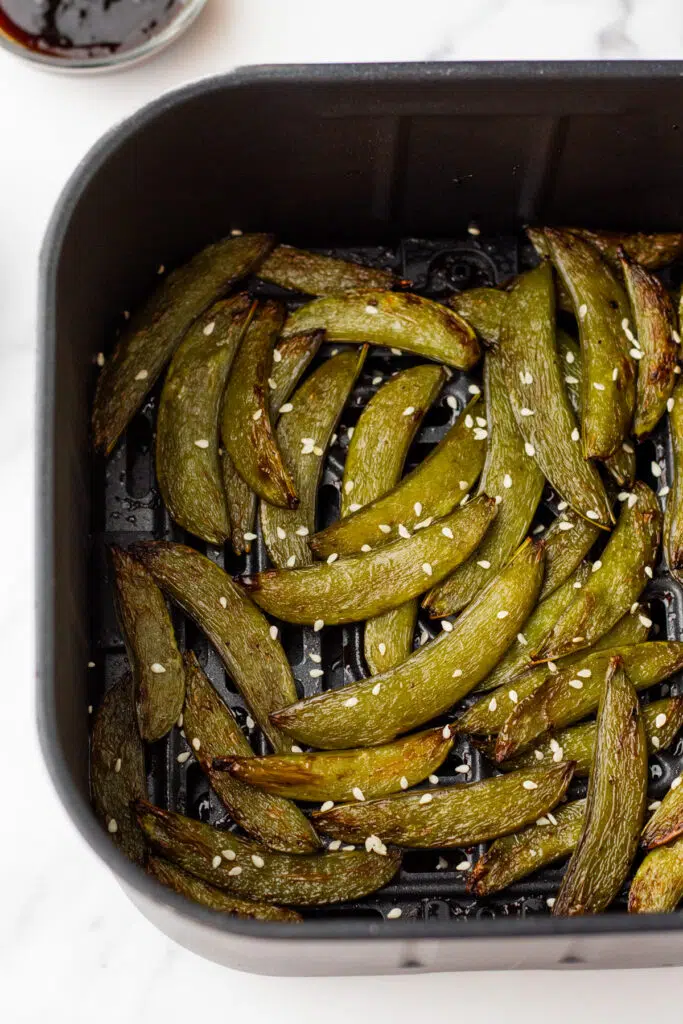 Close up of air-fried sugar snap peas with sesame seeds in an air fryer basket