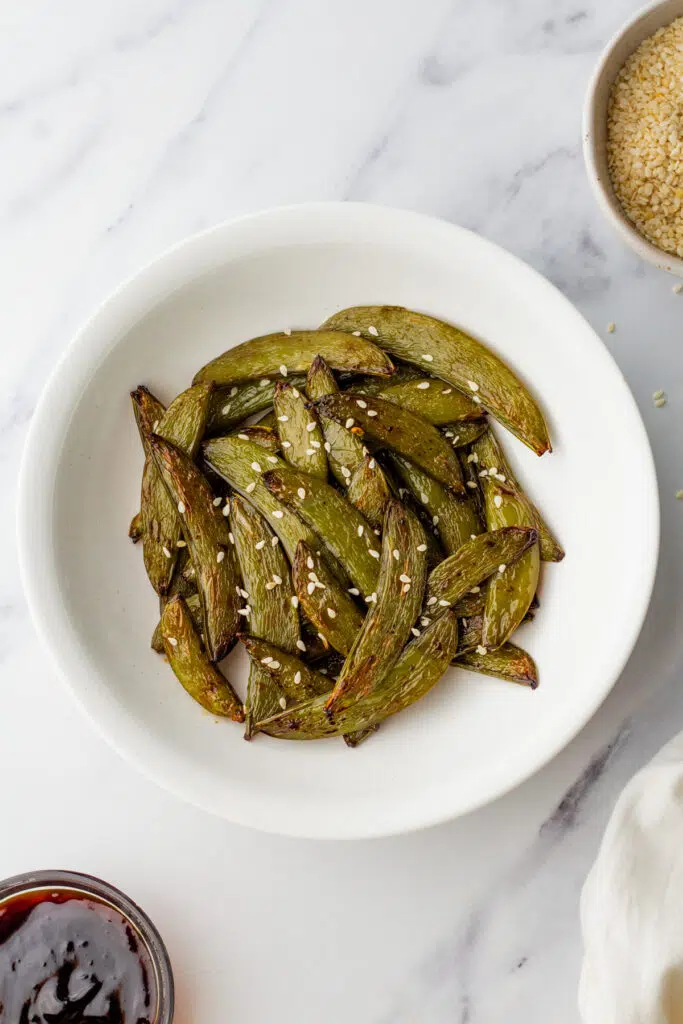 Air-fried snap peas with sesame seeds in a white bowl.