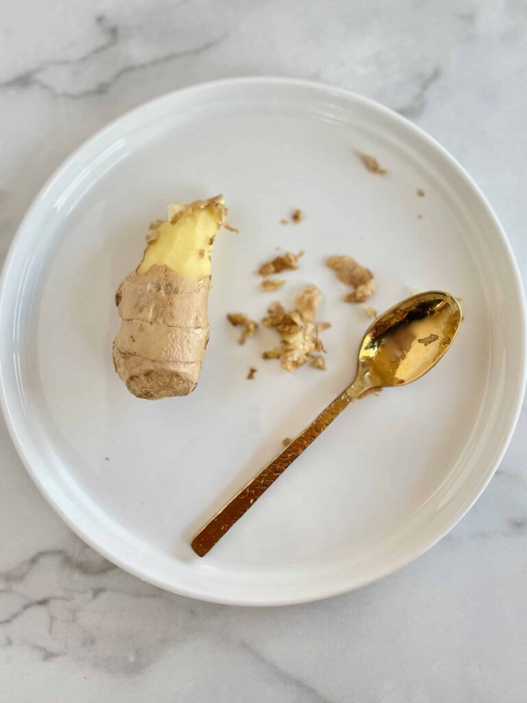 Close up of half peeled ginger and a gold spoon