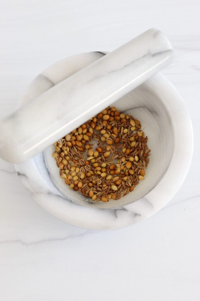 Whole coriander and cumin seeds in a mortar and pestle