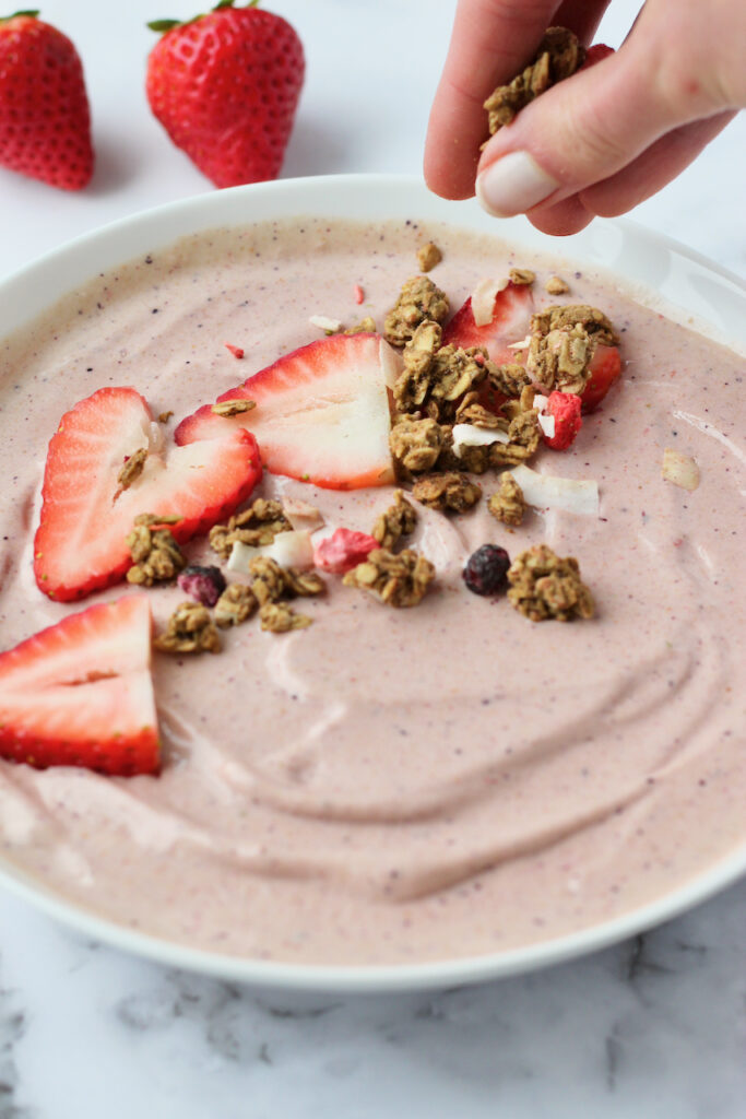 Topping strawberry smoothie bowl with granola
