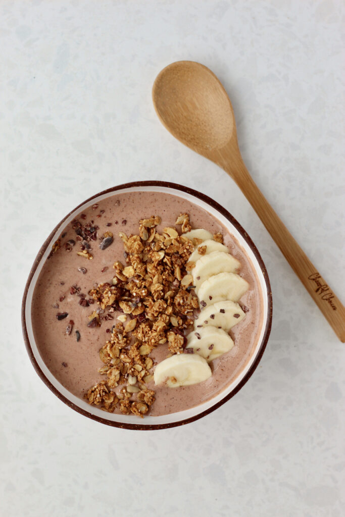 Chocolate smoothie bowl in coconut bowl next to wooden spoon