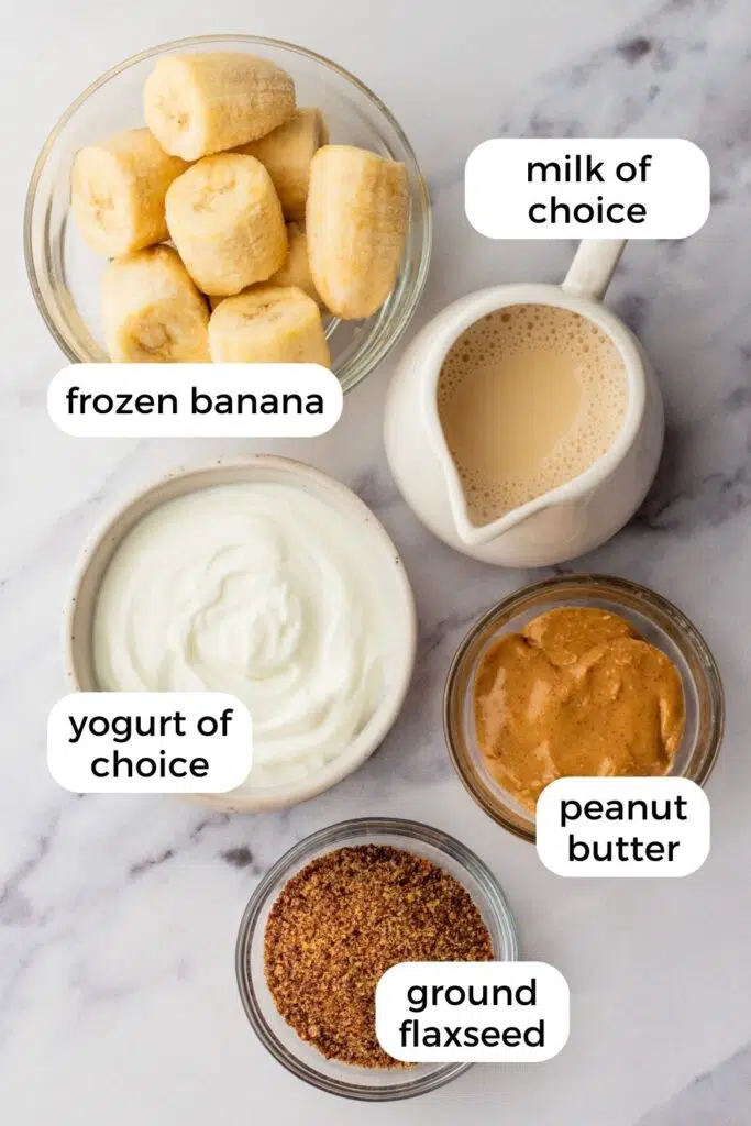 Ingredients for a flaxseed smoothie—frozen bananas, peanut butter, yogurt, and milk—on a marble surface.