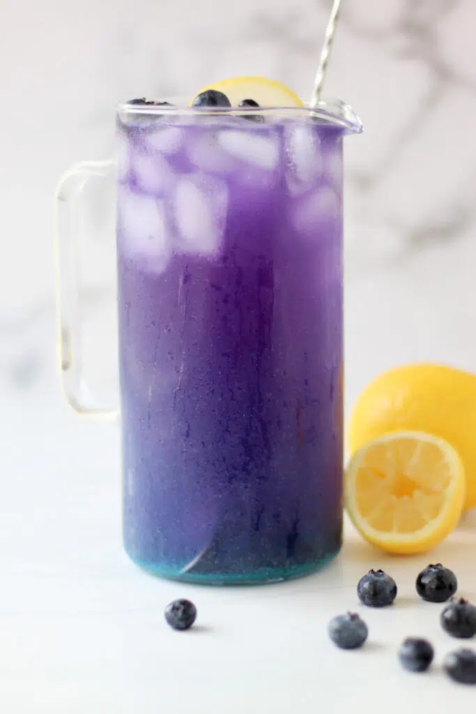 Tall pitcher filled with butterfly pea lemonade and topped with fresh blueberries