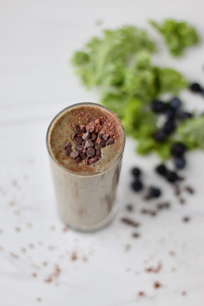 Chocolate smoothie with kale and blueberries in the background