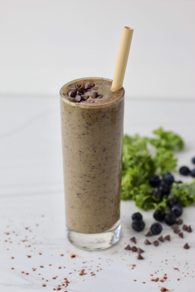 Chocolate smoothie with bamboo straw with kale and blueberries in the background
