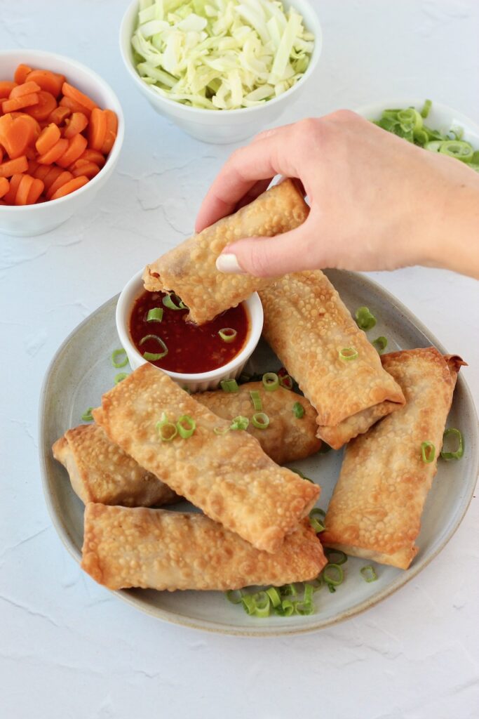 Hand dipping air fryer egg roll in sauce