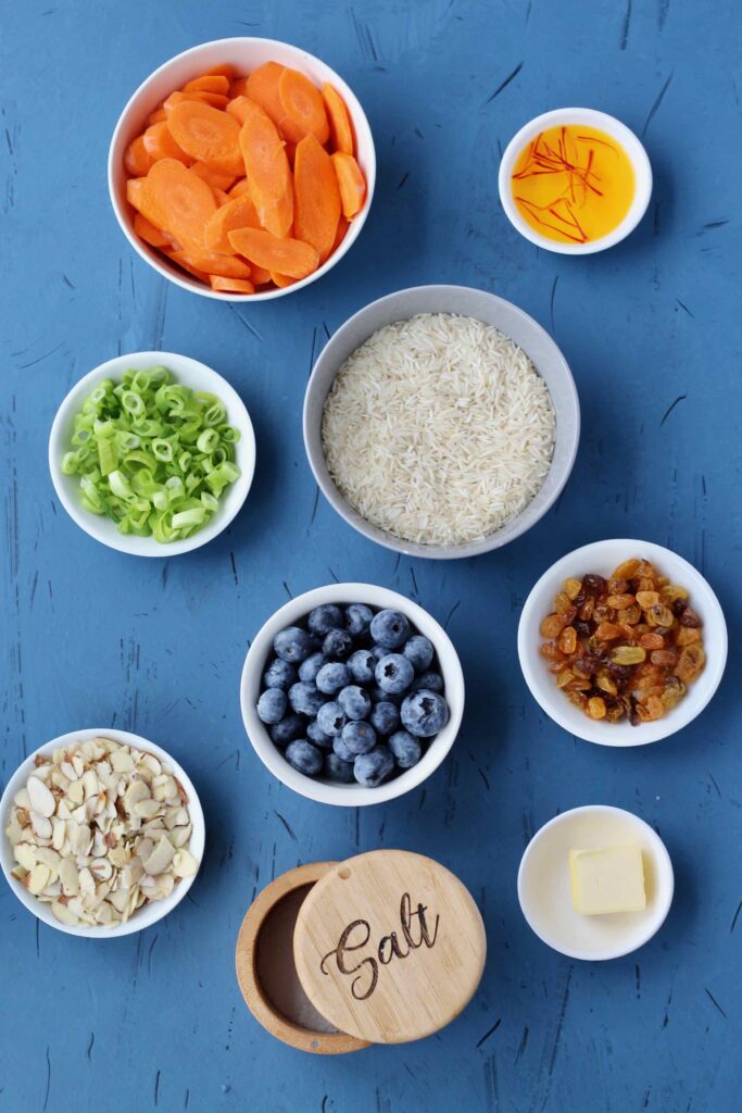 Green onions, blueberries, carrots, raisins, almonds laid out on blue backdrop