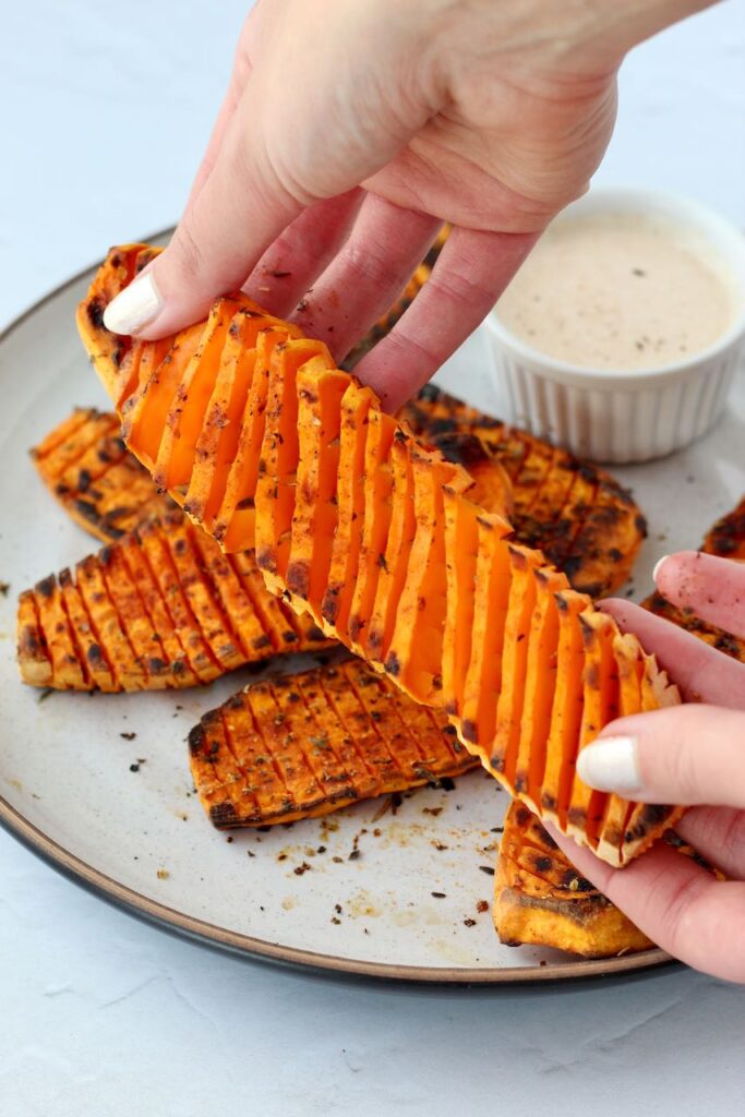 Pulling apart accordion-cut sweet potatoes on a plate with smoked paprika aioli.