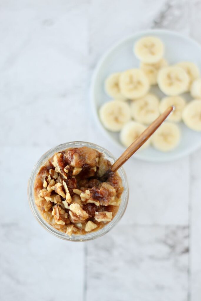 Taking spoonful of creamy overnight oats with banana slices and walnut topping