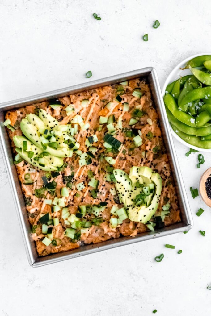 Sushi bake in a pan garnished with avocado and green onions.