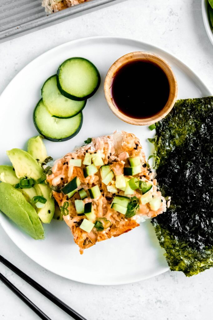 Sushi bake slice on plate with avocado and soy sauce.