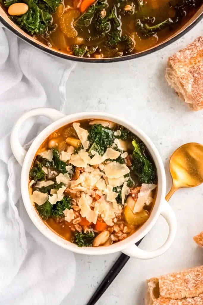 A bowl of Tuscan white bean and farro soup topped with shaved parmesan and kale.