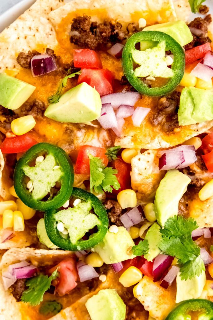 A close up of a tempting dish of layered nachos with cheese, diced vegetables, and spicy jalapeños.