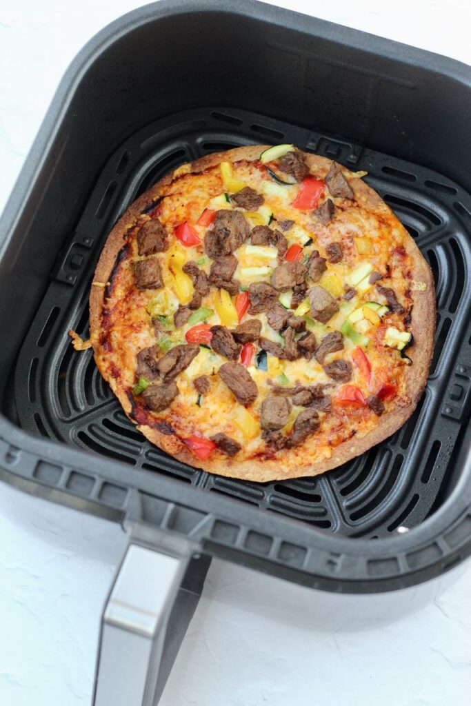 Air fryer tortilla pizza with cheese and vegetable toppings.