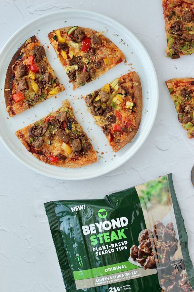 Sliced tortilla pizza with Beyond Steak and colorful vegetables.