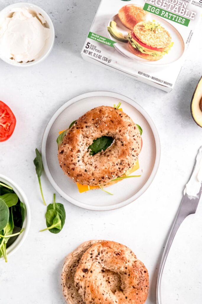  hearty and healthy sandwich with a toasted multigrain bagel, filled with egg, cheese, fresh tomato, and spinach on a simple plate.