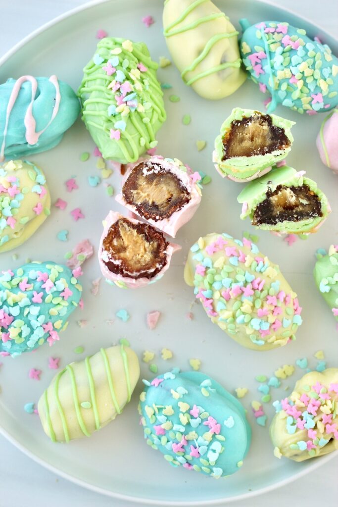 A plate of colorful Medjool date peanut butter eggs coated in pastel-colored chocolate and adorned with spring-themed sprinkles