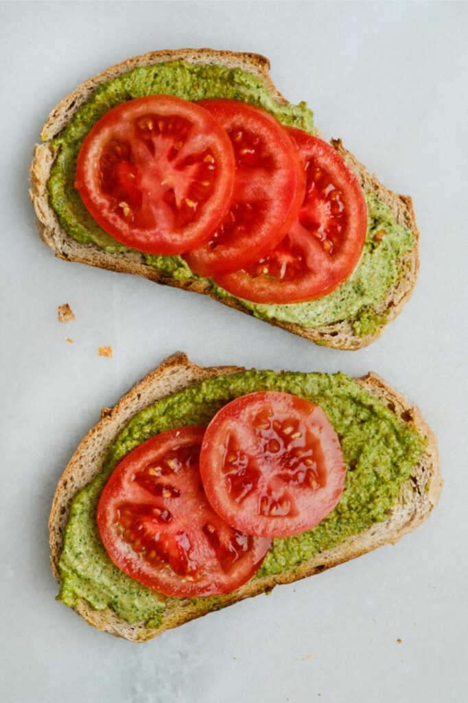 Pistachio pesto toast on a slice of bread with sliced tomatoes.