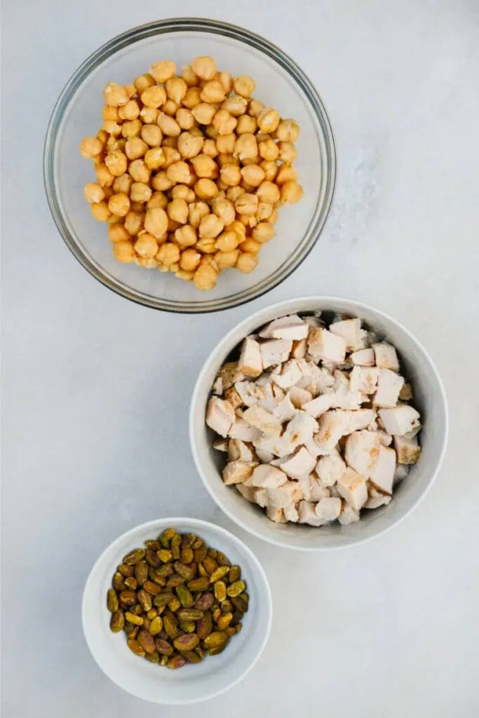 Chickpeas, chopped chicken, and pistachios in separate bowls.