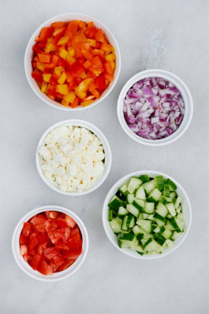 Chopped peppers, onion, cucumber, tomato, and feta cheese in separate bowls