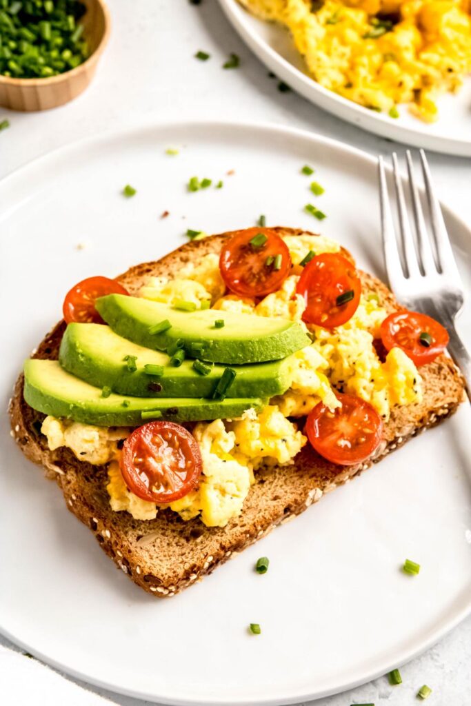 Whole grain toast with scrambled eggs, sliced avocado and sliced tomatoes on top