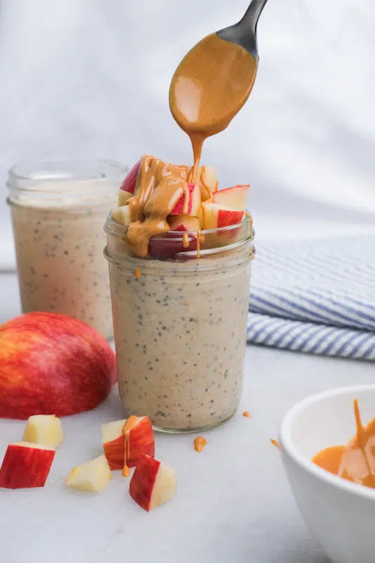 Drizzling peanut butter over apple toppings on blended overnight oats