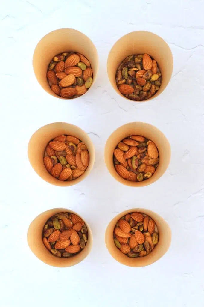 Six individual charcuterie cups with nuts at bottom