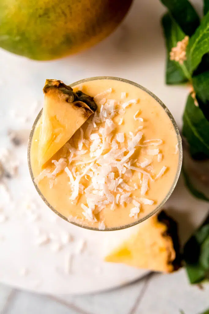 Birds eye view of yellow smoothie with coconut flakes and a pineapple slice on top.