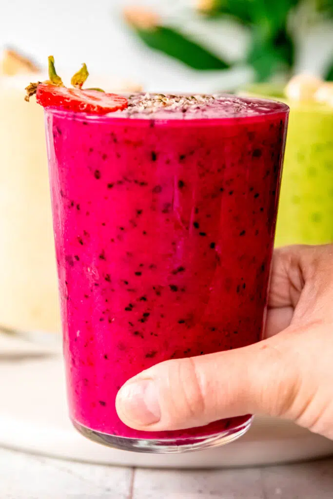 Hand holding bright pink smoothie with a strawberry slice on rim.