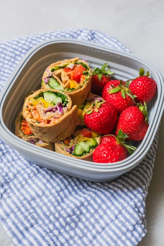 Colorful veggie pinwheels in meal prep container with strawberries