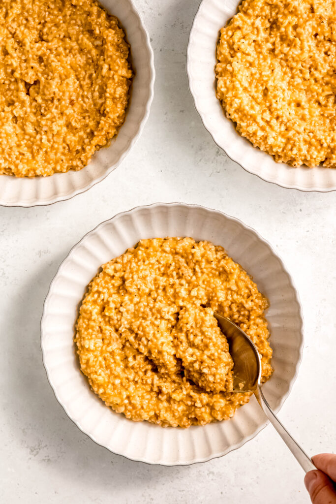 Three dishes of plain savory oats in white bowls. Scoop is being taken out of one.