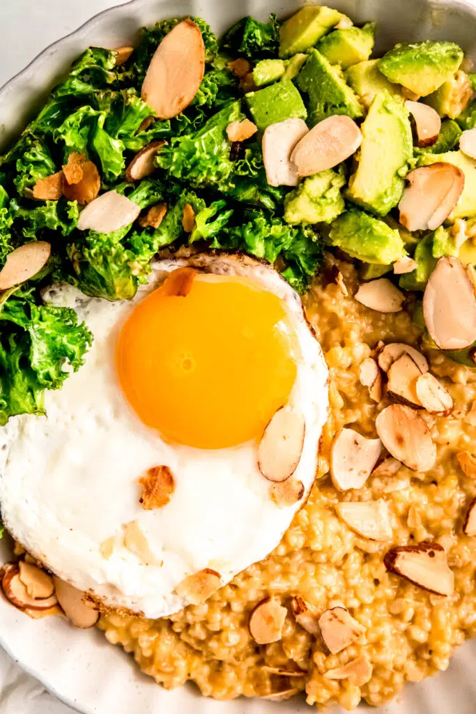 Savory oats with sunny side up egg, greens, avocado, and almonds in white bowl.