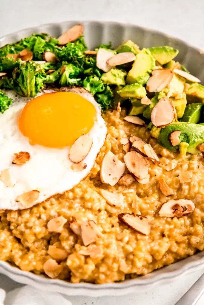 Savory oats with sunny side up egg, greens, avocado, and almonds in white bowl.