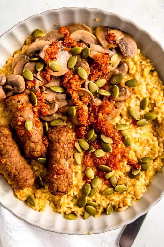 Savory oats with sausage links, mushrooms, and sunflower seeds in white bowl.