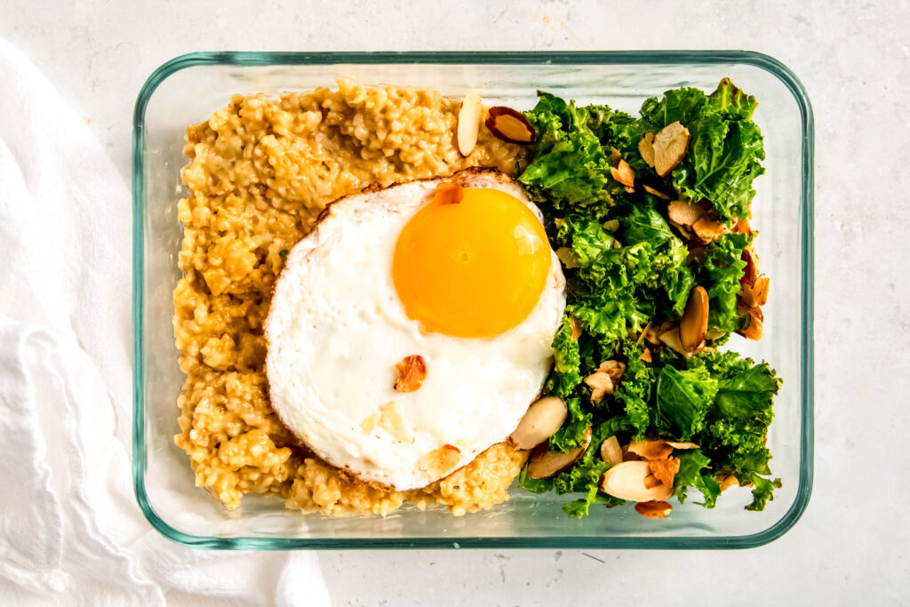 Savory oats with sunny side up egg, greens, avocado, and almonds in storage container.