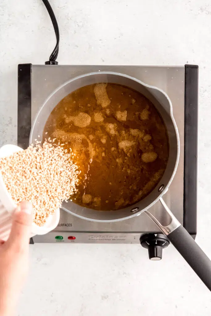 Pouring uncooked steel cut oats into vegetable broth on the burner.