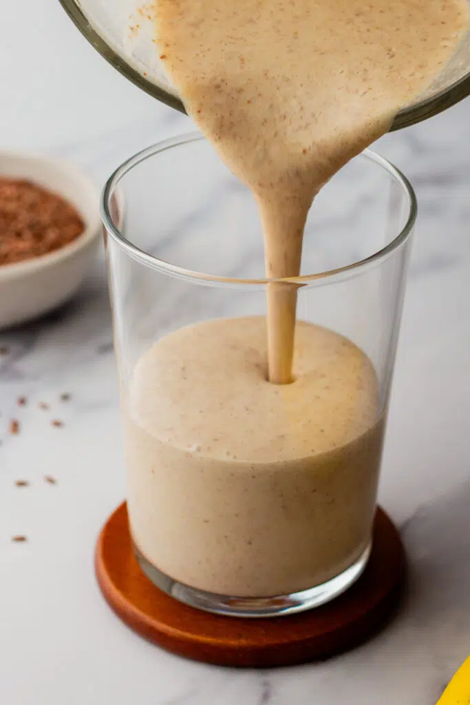 Pouring a thick, creamy protein smoothie into a glass.