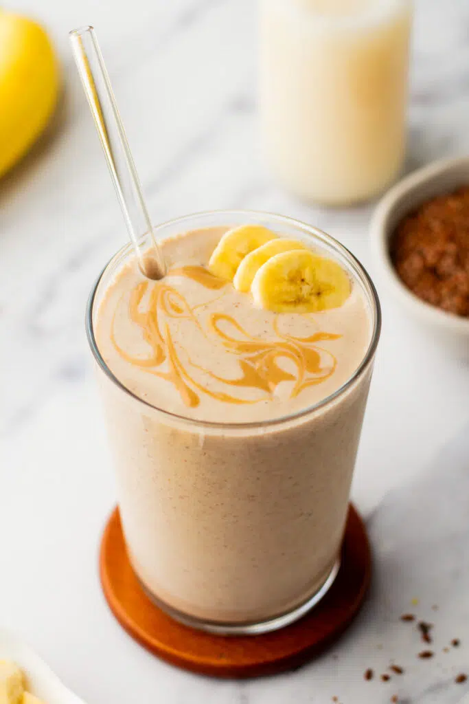 A glass of flaxseed smoothie topped with banana slices and a peanut butter swirl.