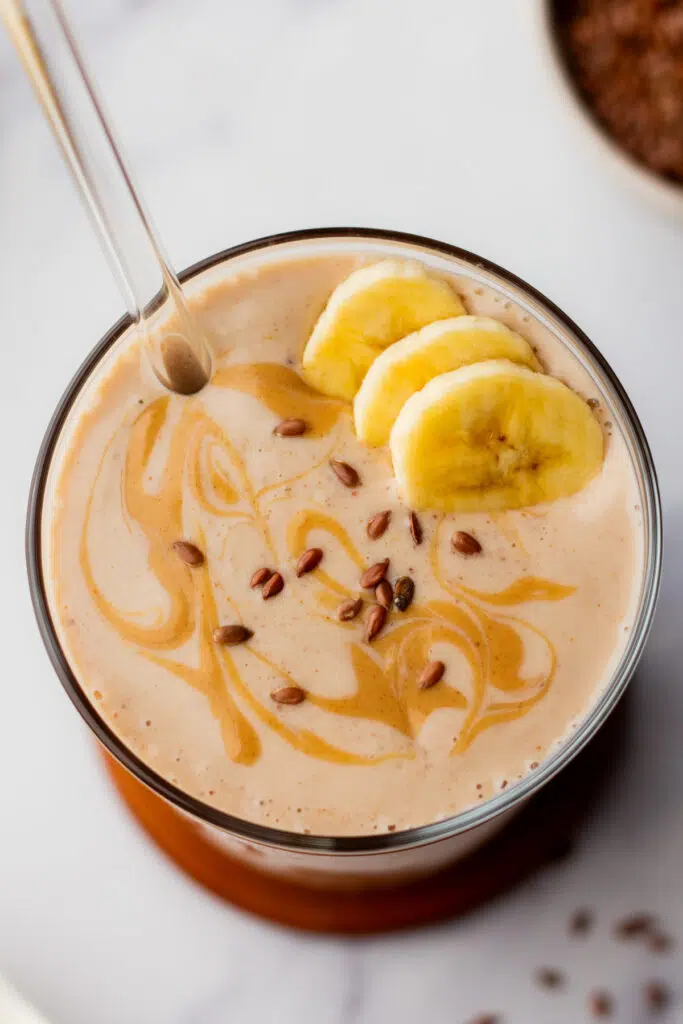 A flaxseed smoothie in a glass with banana and peanut butter, next to smoothie ingredients.