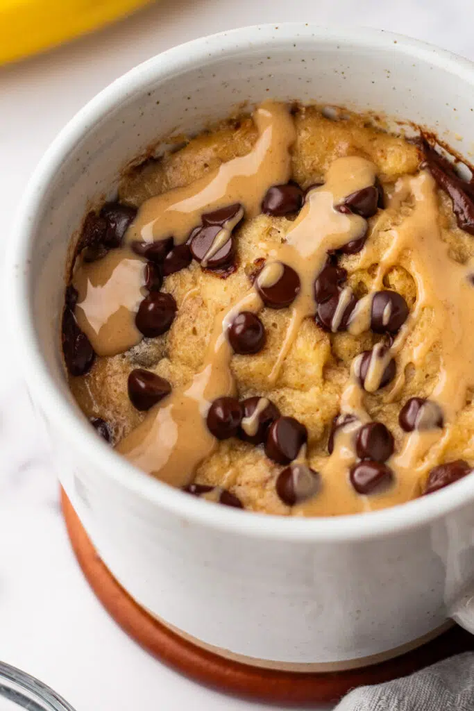 Close-up of a protein powder mug cake with chocolate chips in a white ceramic mug. Learn how to make this fluffy and satisfying chocolate protein mug cake with simple ingredients.