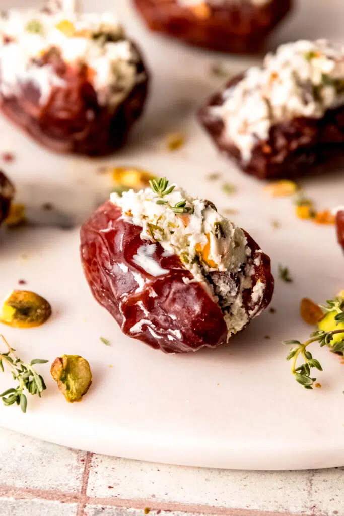 Close up of goat cheese stuffed date with fresh herbs and pistachios around.