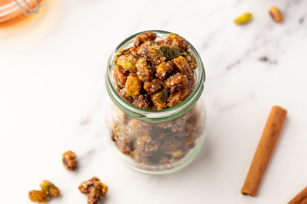 Air fried honey roasted pistachios in cute jar with cinnamon sticks around