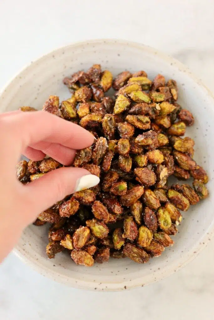 Hand grabbing honey roasted pistachios from bowl