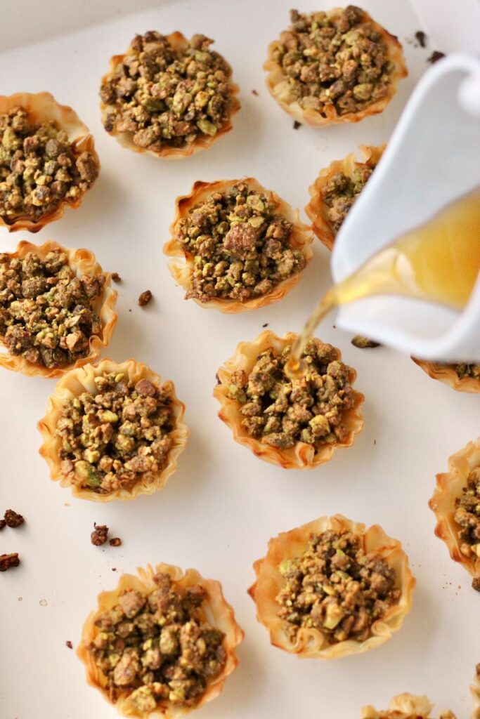 Honey being drizzled over golden pistachio baklava bites