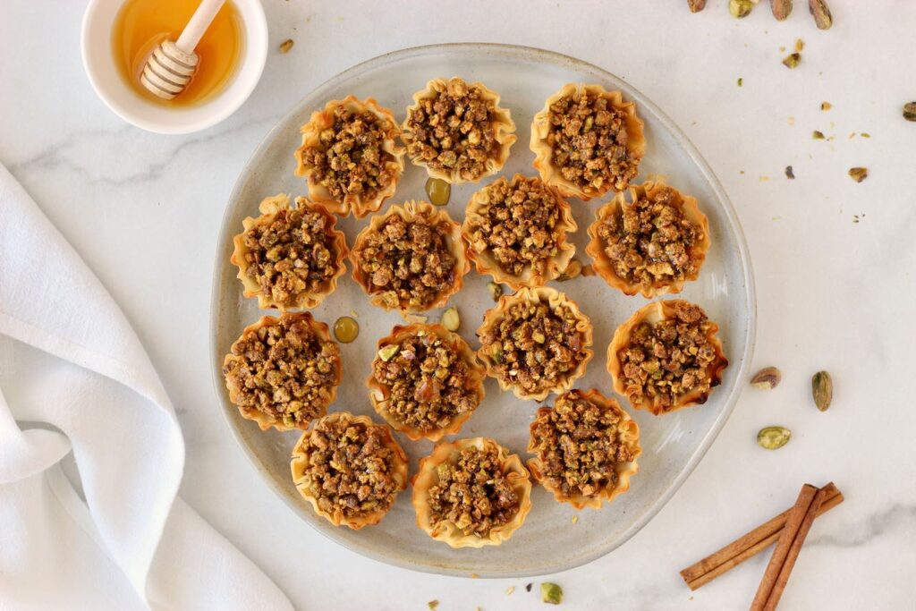 Pistachio baklava bites on grey plate with honey drizzle and cinnamon sticks