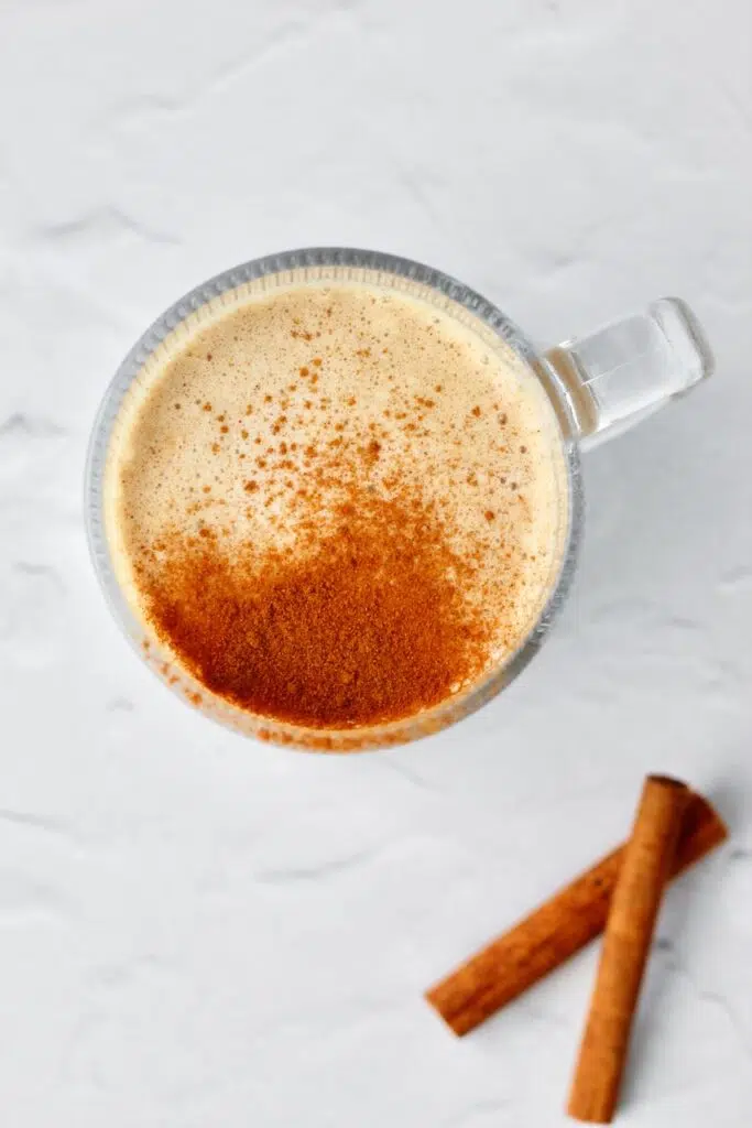 Cinnamon roll protein latte with cinnamon sticks on side