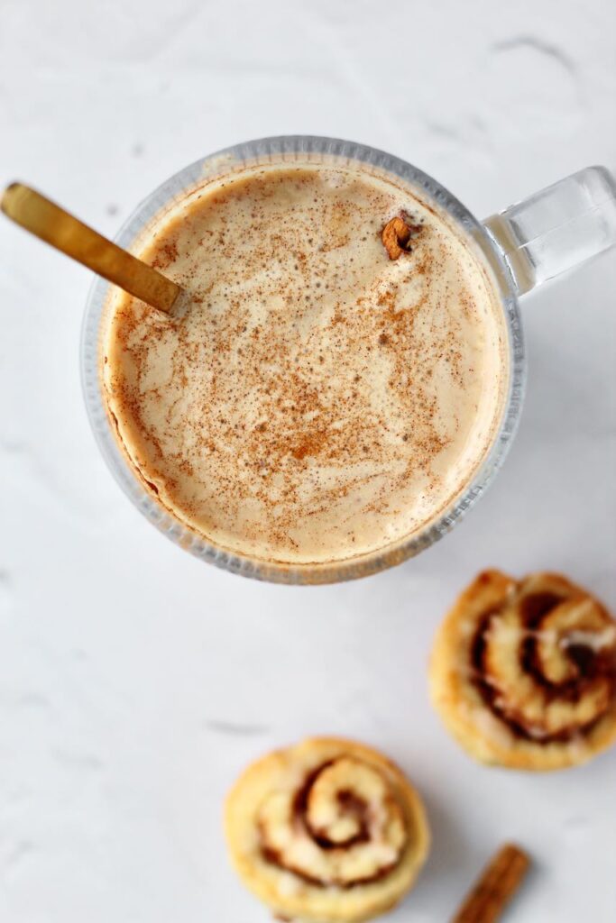 Cinnamon roll protein latte with  cinnamon rolls in background